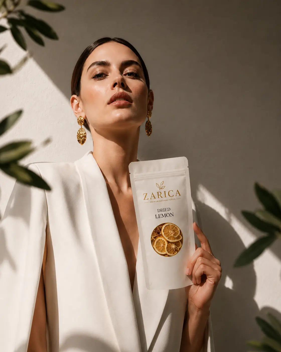 Model in an ivory suit holding a ZARICA dried lemon pouch in warm natural light